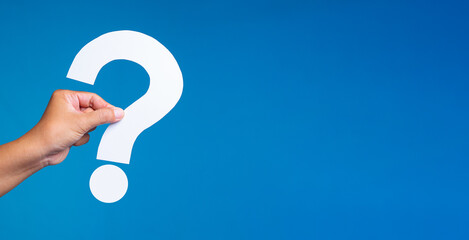 Hand holding white paper question mark on blue background.