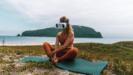 Close-up of woman in sportswear meditating in VR headset on beach with sea view. Modern balance of wellness, technology and nature.
