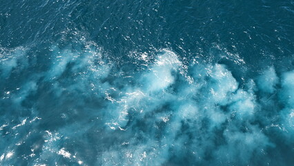 Open sea with deep blue water and white foamy waves left by a moving ship