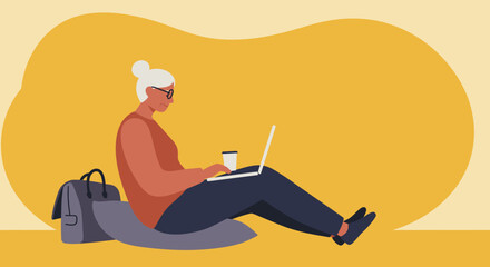 Focused senior woman using laptop and drinking coffee while sitting casually. Represents modern older generation, remote work, learning, and digital lifestyle.