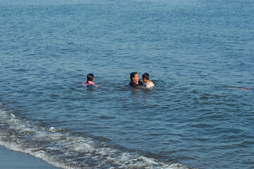 A caring mother assists her son with his clothing while in shallow seawater, surrounded by the cheerful energy of a family beach day.