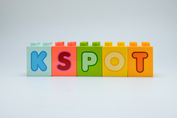Colorful plastic toy blocks spelling the word K SPOT with alphabet letters arranged in a row on white background. Concept of education, learning, childhood creativity, and playful design