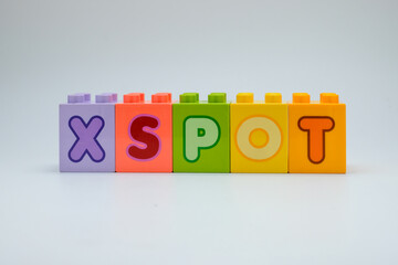 Colorful plastic toy blocks spelling the word X SPOT with alphabet letters arranged in a row on white background. Concept of education, learning, childhood creativity, and playful design