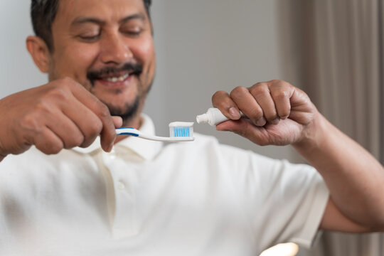 Smiling man squeezing toothpaste on toothbrush preparing for brushing teeth oral hygiene dental care habit