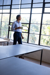 Businessman standing by large windows, holding glasses, contemplating outside view