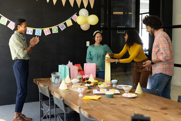 Colleagues celebrating baby shower in office, exchanging gifts and enjoying snacks
