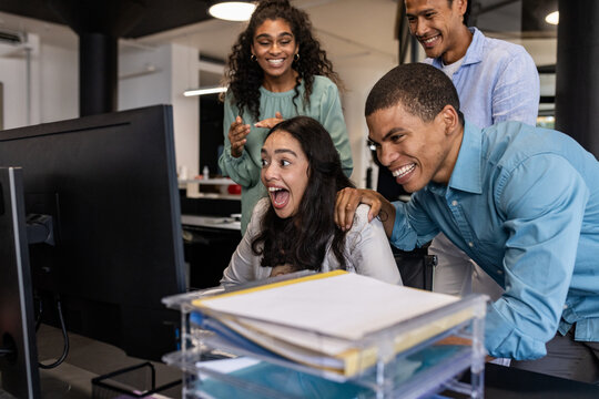 Diverse business team celebrating success while looking at computer in modern office