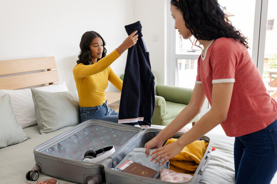 Organizing clothes and essentials, two women packing suitcase at home for trip
