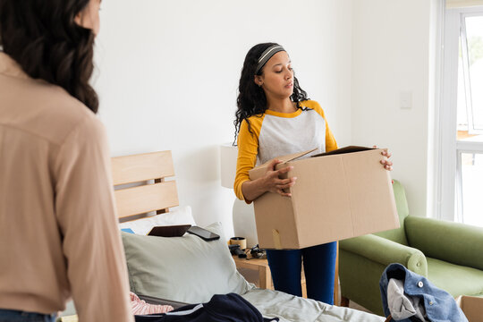 Woman carrying cardboard box in bedroom while organizing and tidying up space