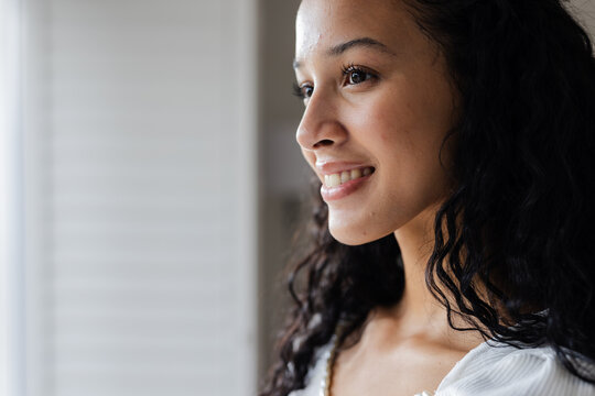 Smiling woman looking out window, feeling hopeful and inspired at home