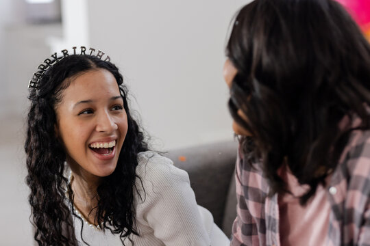Celebrating birthday, smiling woman wearing tiara talking with friend at home
