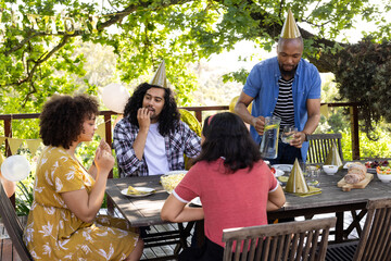 Celebrating birthday outdoors, friends wearing party hats and sharing snacks together