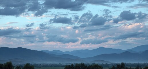 Soft morning landscape. Layered mountains under a soft pastel sky filled with clouds, view from afar over a field