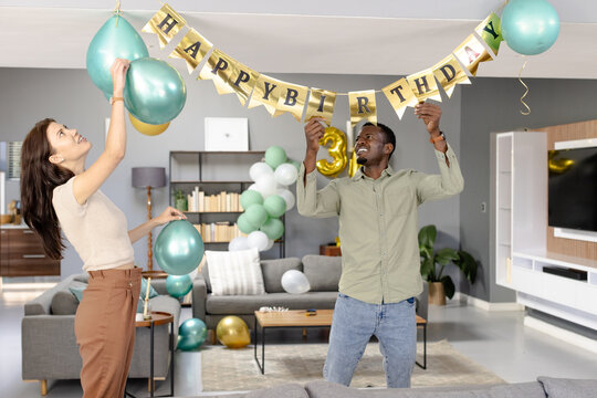 Friends decorating living room with balloons and banner for birthday celebration