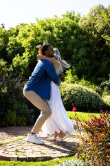 Couple joyfully dancing together in sunny garden, surrounded by lush greenery
