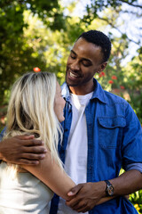 Couple embracing outdoors, smiling and enjoying sunny day in park
