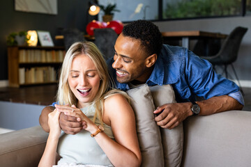 Couple at home laughing together while looking at smartphone on couch