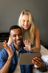Smiling couple video chatting on tablet, waving and enjoying conversation at home