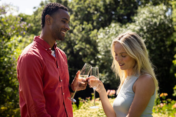 Couple celebrating outdoors, toasting with champagne glasses in sunny garden