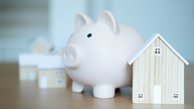 Piggy bank beside wooden house model reflecting financial growth, property investment, and secure savings for future housing.