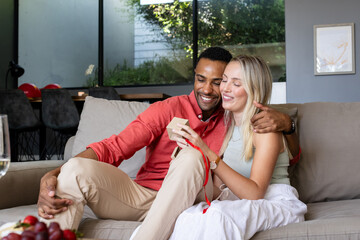 Couple exchanging gifts on sofa, smiling and enjoying cozy moment at home