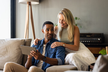 Happy couple using tablet together on couch, enjoying relaxed time at home