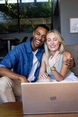 Happy couple video chatting on laptop at home, waving and smiling warmly