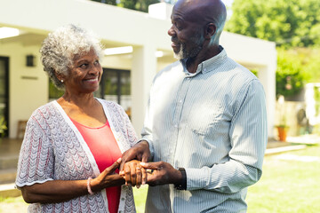 Elderly couple holding hands and smiling warmly in sunny garden