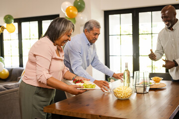 Smiling adults arranging snacks and drinks on table during festive gathering at home