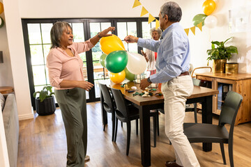 Decorating dining room with colorful balloons, elderly couple preparing for celebration