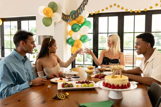 Friends celebrating birthday at home, enjoying food and raising glasses in cheer