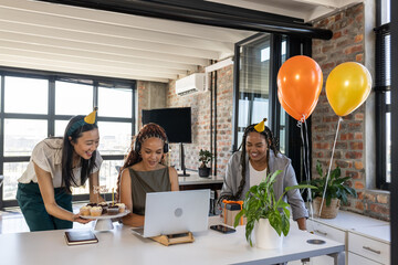 Celebrating birthday in office with cupcakes and balloons, colleagues smiling together