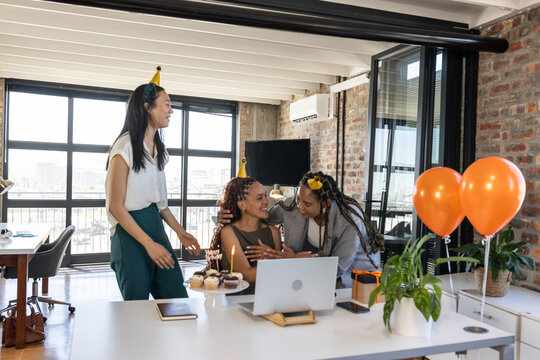 Celebrating birthday in office, colleagues wearing party hats and holding cupcakes - Powered by Adobe