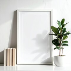 A blank white frame sits on a shelf with books & a potted plant against a white wall, with sunlight creating soft shadows