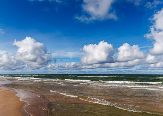 Nordic sea shoreline with gentle waves under blue sky and white cumulus clouds, calm and natural coastal scene, perfect for travel, tourism, relaxation and nature landscape projects