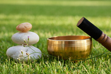 A Tibetan singing bowl and stacked zen stones on green grass, a concept for sound healing and...