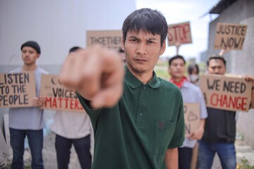 Young Asian Man Pointing At Camera And Conveying Strong Call To Action During Protest