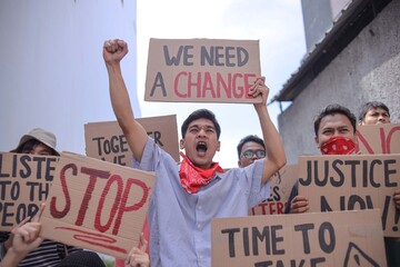 Group Of Young Protestors Yelling And Raising Fist While Holding Sign During Protest