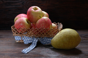 Ripe red apples in a basket with a ripe pear on a wooden table