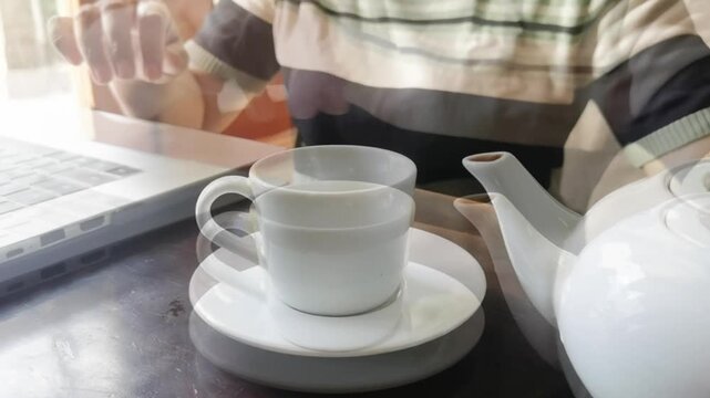 Pouring tea while working on laptop. Cozy breaktime scene with beverage preparation and technology.