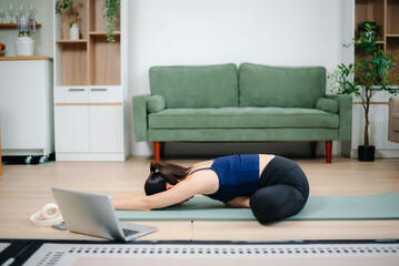 Young Asian woman practicing yoga indoors on a mat. Calm, healthy lifestyle, stretching, wellness and fitness at home