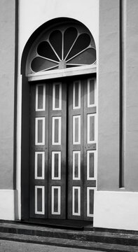 A timeless black and white photograph capturing the entrance of a building, where shadows and light play across textured walls and architectural details.
