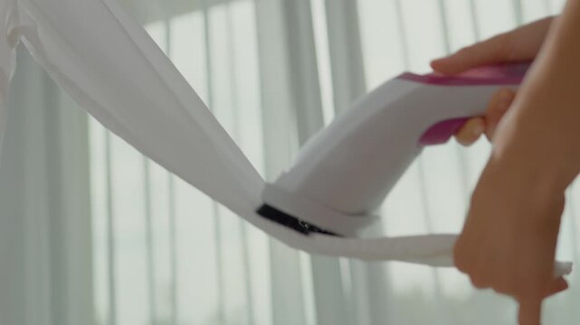 A person uses a clothing steamer to carefully eliminate wrinkles from a delicate garment, ensuring it looks fresh and ready for wear in a bright, airy space.