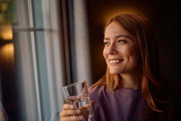 Happy woman with glass of water by window.