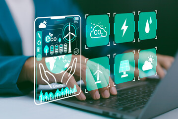 Hands on laptop, with a futuristic GUI displaying environmental icons wind turbine, solar, CO2 reduction, energy, water. Sustainable technology, green energy management, and ecological responsibility.