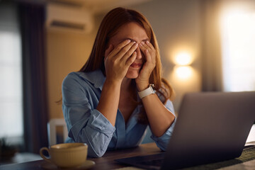 Tired woman rubbing her eyes while working on laptop at home.