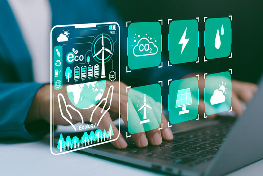 Hands on laptop, with a futuristic GUI displaying environmental icons wind turbine, solar, CO2 reduction, energy, water. Sustainable technology, green energy management, and ecological responsibility.