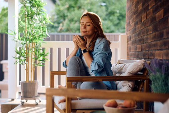 Woman with eyes closed enjoying in smell of fresh coffee on porch. - Powered by Adobe