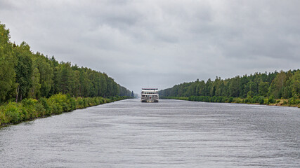 A river passenger ship sails through a canal on the banks of which trees grow