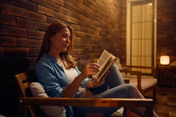 Obraz premium Smiling woman reading book on porch.